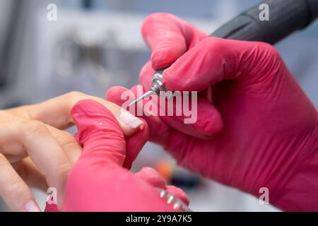 Close up nail technician in pink gloves shapes nails using a drill machine in beauty salon.  Stock Photo