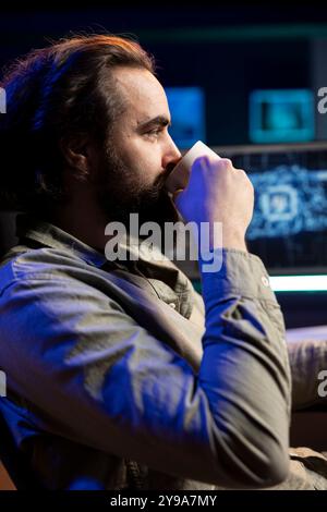 Developer drinking coffee updating artificial intelligence machine learning algorithm on PC desktop at home. IT specialist in apartment office enjoying hot beverage while upgrading AI Stock Photo