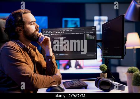 Pensive man doing software quality assurance, carefully analyzing source code on computer screen. Developer thinking of solutions after finding errors while inspecting coding on desktop PC Stock Photo