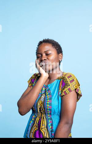 African American model making goofy faces for the camera, radiating confidence and optimism. Delightful enthusiastic woman expressing fun and comical feelings against blue background. Stock Photo