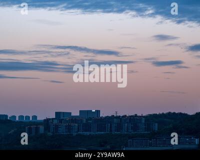 Chongqing city view in sunset, high rise buildings on hills and mountain in the background, clouds lit pink in the sunset light. Stock Photo
