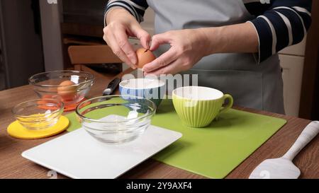 Process of making dough. Woman separates egg white from yolk in kitchen. Scales and eggs, utensils on wooden table. Baking macarons at home. Hands in Stock Photo