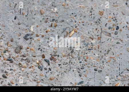 Texture of concrete surface with multicolored pebbles. Monolithic concrete wall with multicolored pebbles, stained with bitumen, high resolution. Stock Photo