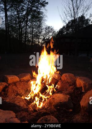 A warm glowing campfire in the Georgia mountainside right by a flowing river at night. Stock Photo