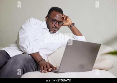 Handsome Black African American Man Working on Laptop Computer while Sitting on a Sofa in Cozy Living Room. Freelancer Working From Home. Browsing Int Stock Photo