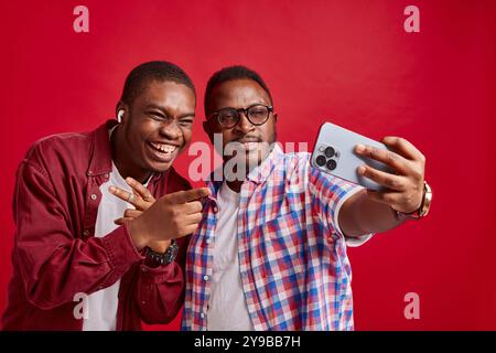 Two young African American men rejoice with their hands outstretched towards the phone camera, isolated on red background Stock Photo