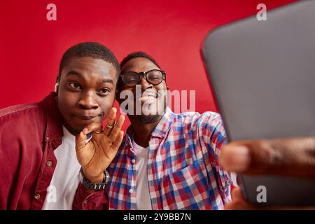 Two young African American men rejoice with their hands outstretched towards the phone camera, isolated on red background Stock Photo