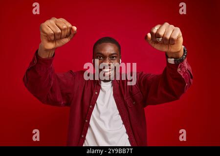 portrait of emotional african american man rejoicing with hands outstretched to camera isolated on red background, studio portrait Stock Photo