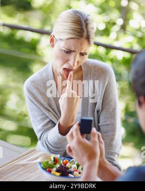 Disgust, upset and couple with engagement ring for proposal in restaurant, cafe and diner. Dating, marriage and man and woman with vomit gesture for Stock Photo
