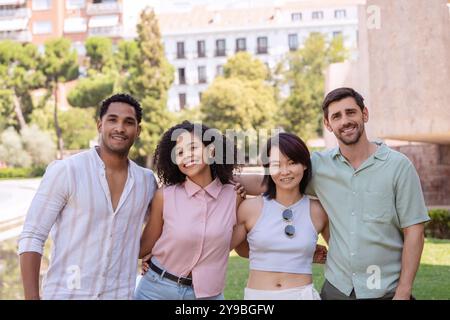 Four friends are posing with their arms around each other while exploring a new city together Stock Photo