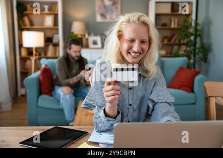 Shopaholic problem. Young business woman working at home in home office taking a break for online shopping on her laptop computer with credit card whi Stock Photo