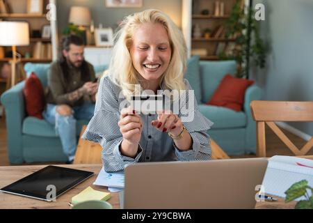 Shopaholic problem. Young business woman working at home in home office taking a break for online shopping on her laptop computer with credit card whi Stock Photo