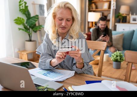 Shopaholic problem. Young business woman working at home in home office taking a break for online shopping on her laptop computer with credit card whi Stock Photo