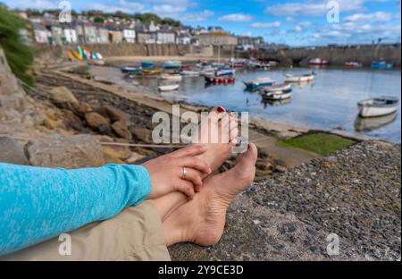 Woman relaxing barefoot at the harbour of Mousehole, Cornwall, on a sunny summer day Stock Photo