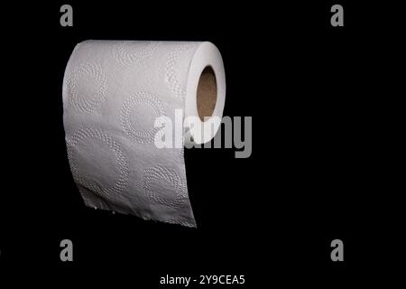 A close-up image of a white toilet paper roll with a circular embossed design, partially unrolled and hanging against a black background. Stock Photo