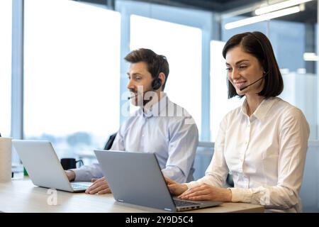 Business professionals using headsets while working on laptops in office setting. Call center employees discussing client communication, focused on providing excellent customer service. Stock Photo