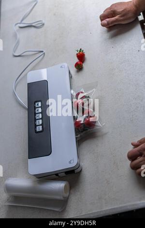 a man's hand is using a vacuum machine to vacuum pack strawberries into plastic bags. . High quality photo Stock Photo