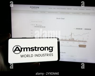 Person holding mobile phone with logo of American company Armstrong World Industries Inc. on screen in front of web page. Focus on phone display. Stock Photo