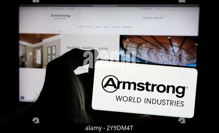 Person holding smartphone with logo of US company Armstrong World Industries Inc. on screen in front of website. Focus on phone display. Stock Photo