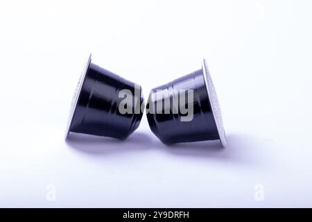 Two black coffee capsules placed on a pristine white surface, showcasing their sleek design and rich coffee essence Stock Photo