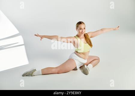 A sporty woman performs a graceful split in a bright studio, showcasing her strength and flexibility. Stock Photo