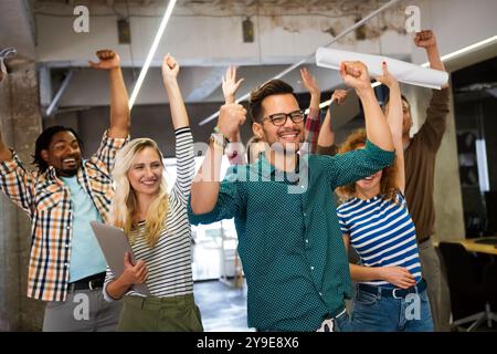 Happy young successful business team celebrating a triumph with arms up in startup office. Stock Photo