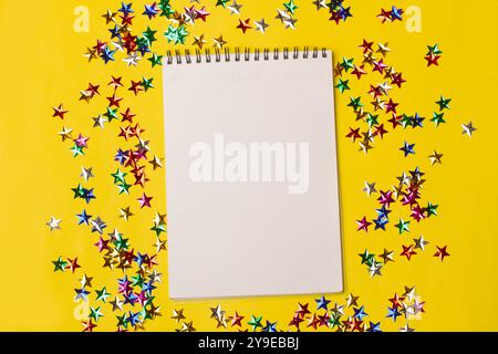 An open notebook on a blank page on a yellow background with shiny colored stars Stock Photo