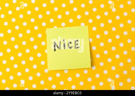 Nice single word written on a yellow adhesive note on a yellow with white polka dots background Stock Photo
