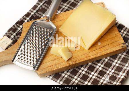 A piece of Parmesan cheese with a cheese grater on a wooden kitchen board on a chequered napkin Stock Photo