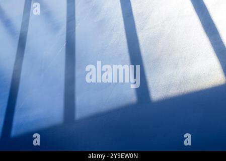 Soft shadows of vertical bars stretch across a smooth blue surface, creating a minimalist and serene atmosphere. Stock Photo