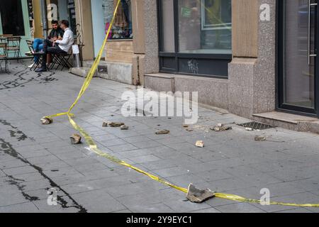 Two men relax at a café table, unfazed by the chunks of masonry that have fallen from the nearby Adriatica Trieste Block, an old building in Bucharest Stock Photo
