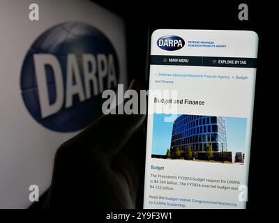 Person holding cellphone with webpage of Defense Advanced Research Projects Agency (DARPA) on screen with logo. Focus on center of phone display. Stock Photo