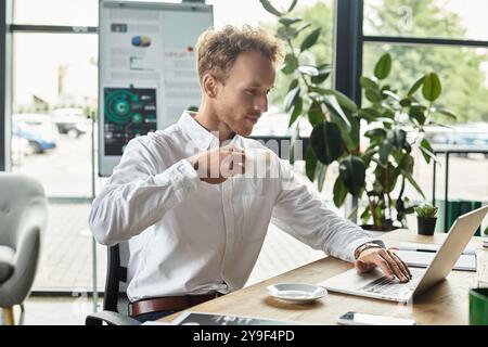 A focused redhead works on his laptop, enjoying coffee in a contemporary office filled with greenery. Stock Photo