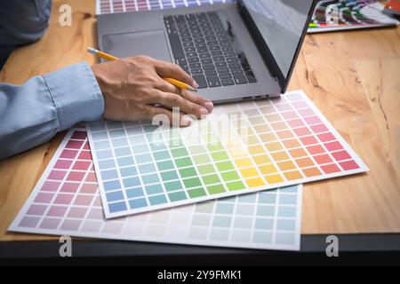Photographer Graphist designer working on a laptop with colors chart. Male designer choosing color swatch samples. Stock Photo