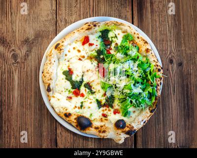 Artisanal Neapolitan-style pizza topped with melted cheese and pesto on one half and fresh arugula leaves with parmesan shavings on the other. Stock Photo