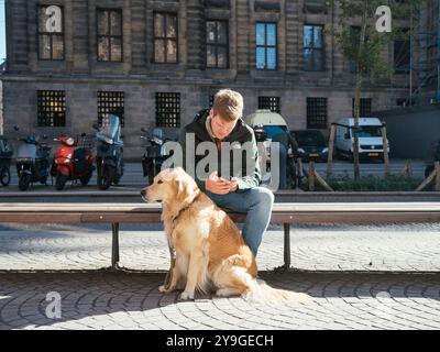Young man scrolling on phone while his dog is patiently sitting in front of him. Stock Photo