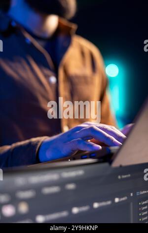 Teleworking programmer doing software debugging using laptop, checking flaws in lines of code displayed on PC monitors. IT admin in apartment fixing coding issues using notebook, close up Stock Photo