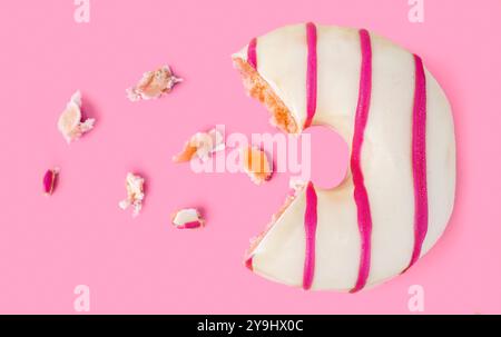Missing piece of white chocolate and pink stripes  donut with crumbs on pink background. Stock Photo