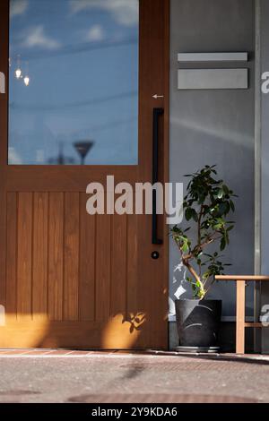 Modern in design, a cream colored entrance to a building is adorned by a light brown colored wooden door with a large glass pane reflecting the sky. Stock Photo