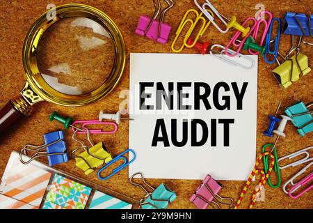 Energy Audit text on paper card with magnifying glass and stationery on cork board background Stock Photo