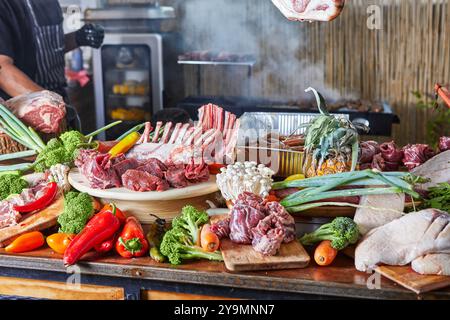 A vibrant display of raw meats, vegetables, and spices, ready for cooking and grilling, set on a rustic table. Stock Photo