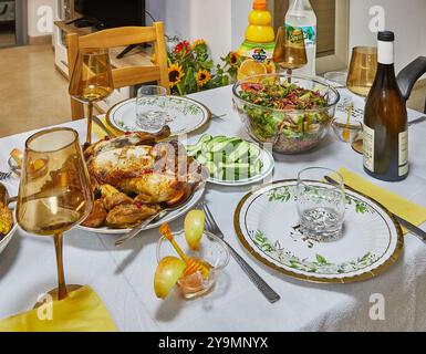 A table set for a festive meal, featuring a range of dishes including roasted chicken, salad, drinks, and elegant tableware. Stock Photo