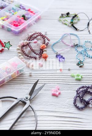 Various beads, charms, and tools are scattered across a wooden table as an artist designs unique pieces of jewelry in a vibrant crafting session. Stock Photo