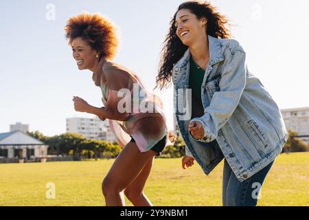 Happy female friends dancing together outdoor in a sunny park, enjoying their fun and carefree moments. Stock Photo
