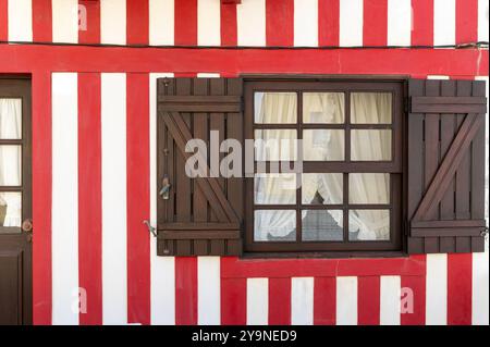 A vibrant striped house features a window with wooden shutters and lace curtains. Stock Photo