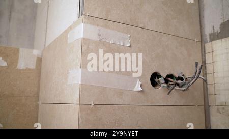 Electrician is working on installing a light switch and socket on a bathroom wall with recently installed tiles Stock Photo
