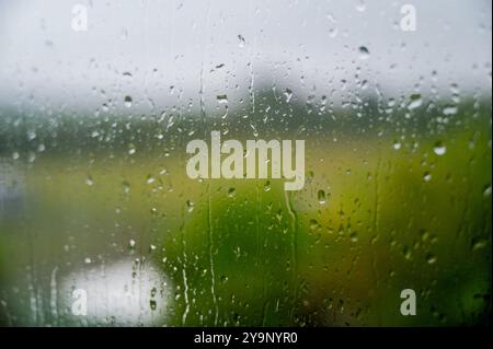 rain drops run down a window pane with out of focus gardens beyond Stock Photo