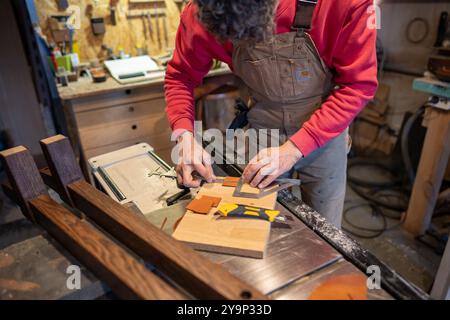 Carpenter work in furniture workshop, using ruler, caliper to cut leather for gluing to bed leg base Stock Photo