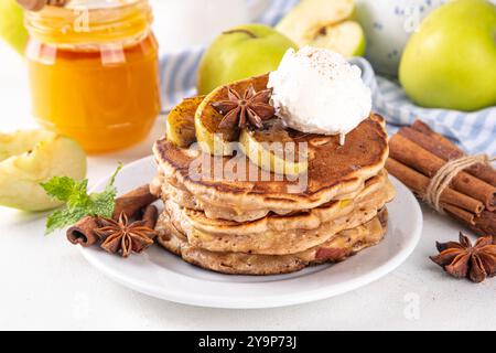 Sweet autumn apple pie pancakes stack with ice cream and caramelized apples on top, won kitchen table with spices, apples and honey jar, copy space Stock Photo