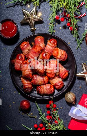 Traditional Christmas dish recipe Pigs in blankets, sausages wrapped in bacon, oven baked puff pastry hot dogs rolls with xmas tree branches, decorati Stock Photo